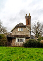 A quaint stone cottage with a chimney and a green lawn.
