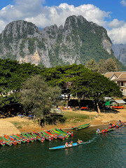 Vertical image of Nam Song River with longtail boats and limestone mountains in Vang Vieng, Laos. Popular riverside tourist destination in Asia.
