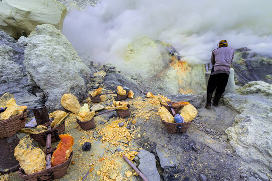Miner working in sulfur mine at volcanic crater surrounded by toxic smoke and yellow sulfur rocks, illustrating dangerous labor, natural resources extraction, geology, and extreme working conditions.