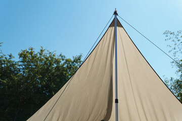 A camping flysheet with poles forming a triangular shape, framed by a forest in the background. A relaxing atmosphere for resting and recharging an adventurer's umbrella.