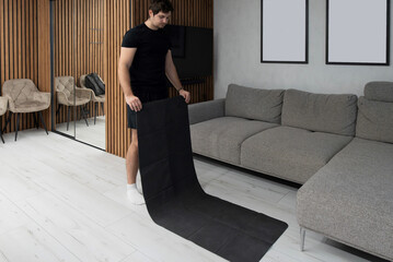 Caucasian man unfolding black yoga mat on floor