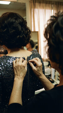 Senior woman helping another woman zip up a sequined dress. Rear view of mature ladies getting ready for a formal event. Female friendship and support concept