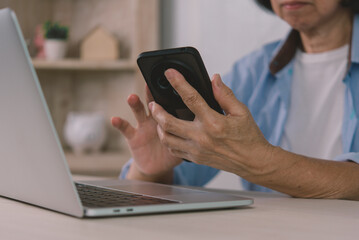 Close up of senior woman hands holding smartphone for two-factor authentication 2FA while working on laptop. Elderly cyber security, online banking verification, and digital identity concept.