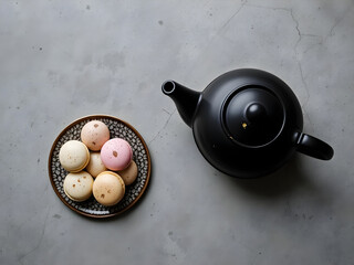 A black tea kettle sits on a table next to a plate of pastries