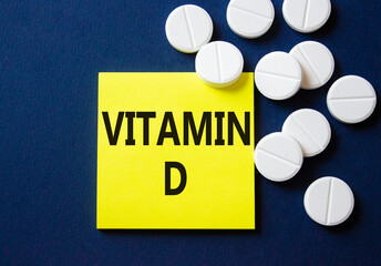 Vitamin D symbol. Concept word Vitamin D on yellow note. Beautiful deep blue background with pills. Medicine and Vitamin D concept. Copy space