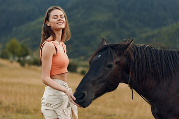 A young woman wearing an orange crop top stands beside a horse in an open field, smiling as the horse nuzzles her hand, creating a calm, intimate moment with nature.