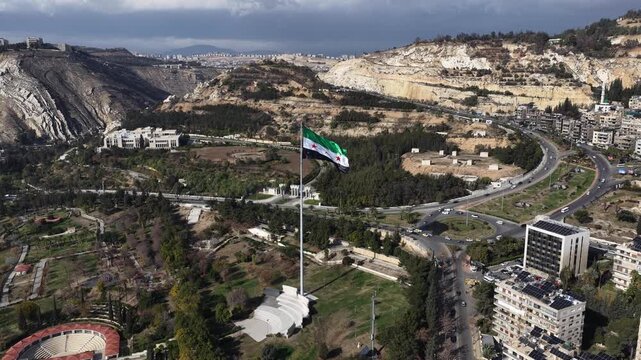 Aerial View of Syrian National Flag Waving on High Flagpole with Mount Qasioun and Damascus Cityscape in Background