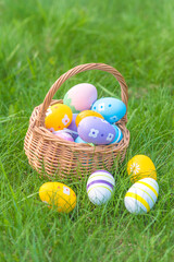 Happy Easter holidays greeting card; wicker basket with easter eggs on a green grass outdoors