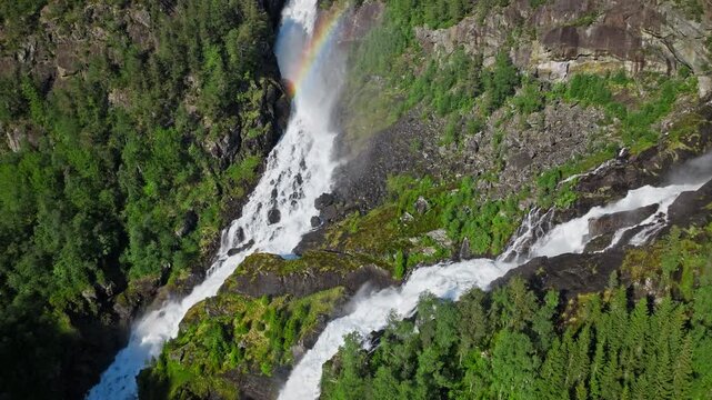 Wide aerial view of Latefossen twin waterfalls in Norway. Scenic summer landscape showing dramatic cascades framed by dense green forest.