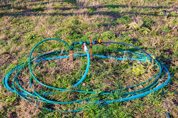 A green garden hose with plastic valves and connectors, coiled on grass for an irrigation system.