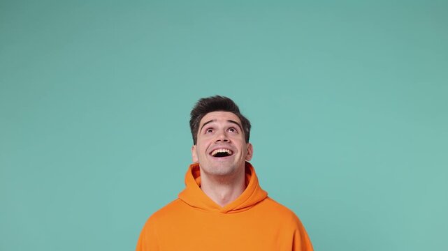 Promoter young man wears orange hoodie point indicate index finger overhead on workspace area copy space mock up isolated on plain pastel light blue cyan background studio portrait. Lifestyle concept