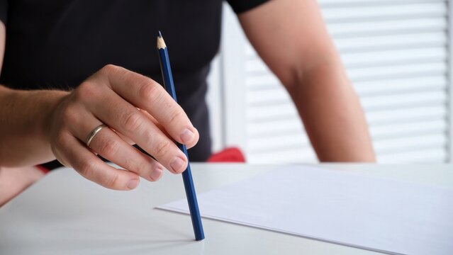 A man tapping a pen on a table with a blank sheet of paper. The concept of lack of ideas, problems, nervous state, lack of inspiration. Beat the rhythm of the melody. Music teacher. High quality.