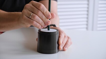 Male hand sticking pencil into automatic electric pencil sharpener and sharpening it close-up side...