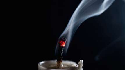 Extinguished candle with smoke trail and glowing red wick on black background. Biblical symbol of fragile faith and prayer. Spiritual concept of hope during Lent.