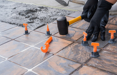 Hand tiler laying tile floor cement glue and rubber hammer, Worker professional furnishing ceramic concrete interior construction house site background.