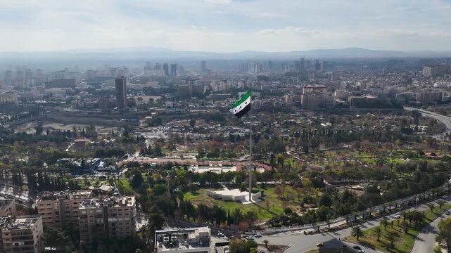 Aerial View of Syrian National Flag Waving on High Flagpole with Mount Qasioun and Damascus Cityscape in Background