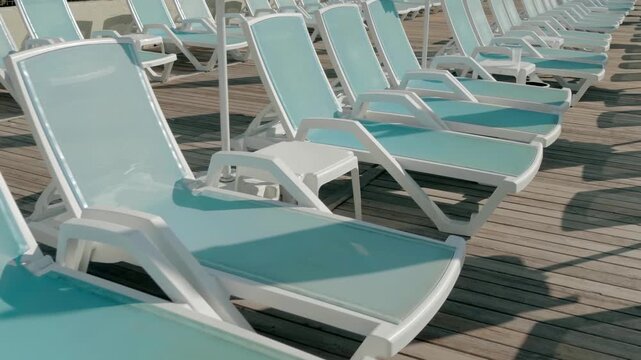 Blue sun loungers are lined up on a wooden pier. It's early morning and there are no sunbathing tourists yet. Shot in motion