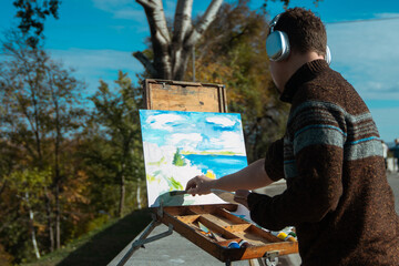 An artist in headphones painting a landscape on a canvas set on an easel outdoors, surrounded by nature.