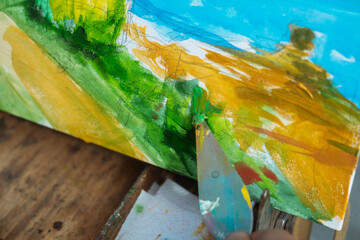 Close up of a colorful landscape painting being crafted with a palette knife, showcasing rich textures.