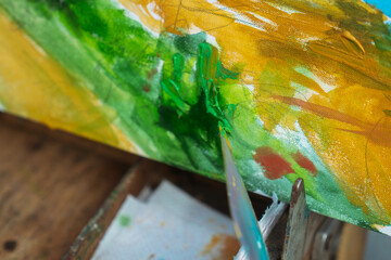 Close up of a colorful landscape painting being crafted with a palette knife, showcasing rich textures.