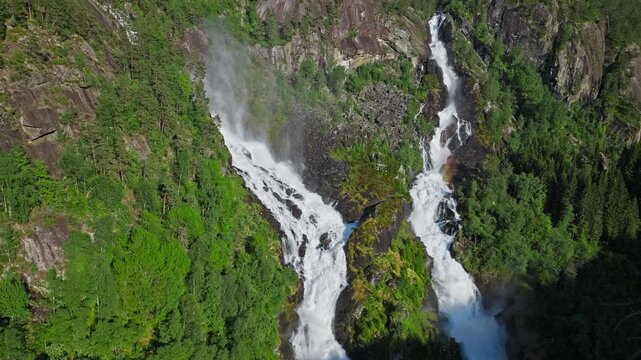 Powerful twin cascades of Latefossen in Norway. Close aerial shot emphasizing fast-flowing water, rugged rock formations, and lush surroundings.