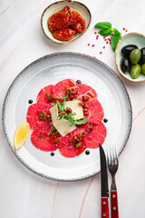 Elegant beef carpaccio with thinly sliced raw wagyu, parmesan shavings, arugula, and balsamic pearls on a marble table. Premium Italian cuisine, gourmet meat starter, luxury beef carpaccio, top view