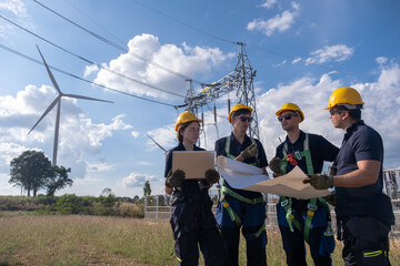 Fototapeta premium Team of workers discussing plans for wind energy project near wind turbines and power lines during daytime