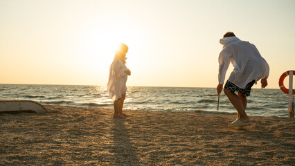 Children play on the beach at sunset. Two children enjoy the sunset on a sandy beach by the sea, casting long shadows and exploring the shallow water, creating memories of a summer vacation.