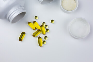 Fish oil capsules. Dietary supplements are scattered across white table, isolated. Set of vitamins for dietary supplements. White table with vitamin capsules and jars