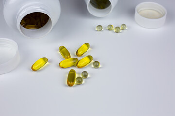 Various types of dietary supplements spill out of jars on white background. Yellow capsules with gelatin membrane for taking vitamins with food. Improving health and wellbeing