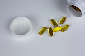 Soft gel capsules spilling from white jar, featuring translucent amber color on white background. Ideal for health, wellness, pharmaceutical or vitamin supplement concept