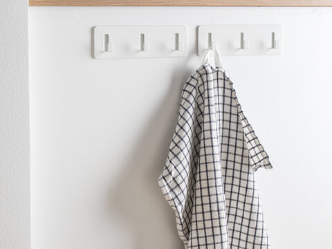 Black and white checkered cotton kitchen towel hanging on a white adhesive wall hook. Absorbent, durable, farmhouse-style dish towel for drying dishes and home use