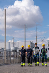 Workers walk along a path at an industrial site with wind turbines in the background during the day