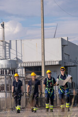 Team of workers walking near industrial site carrying plans during bright afternoon in industrial area