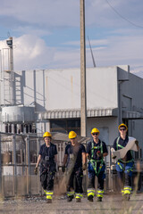 Workers walk on site carrying plans at a facility with machinery in the background during daylight hours in an industrial area