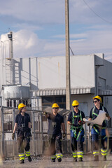 Team of workers walking near industrial site while examining plans during daytime