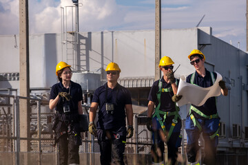 Group of workers walking at a construction site while discussing plans and wearing safety gear during daylight hours