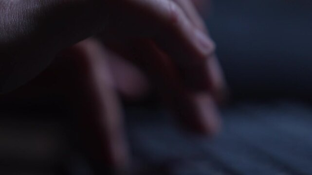 Close up of fingers typing on a keyboard with shallow depth of field. Focus shifts softly as the keys are pressed, showing a quiet moment of computer work in low light.
