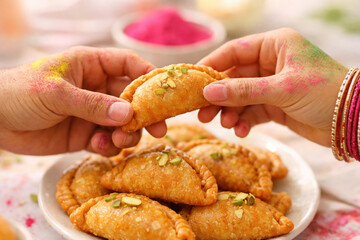 Celebratory hands sharing traditional indian gujiya during colorful holi festival