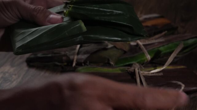 Hands Unwrapping Traditional Raw Tempeh Wrapped in Banana Leaves