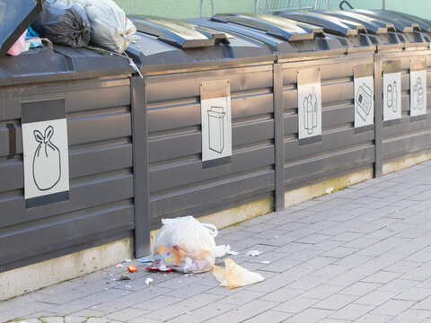 Row of overfilled grey outdoor waste and recycling bins, with litter spilling onto the pavement. Common in Nordic residential areas, showing public misuse and overflow