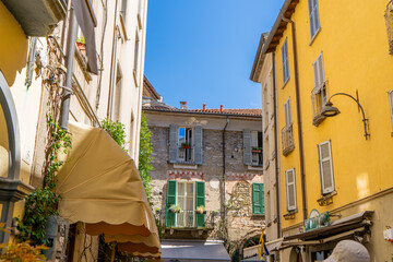 Multicolor windows balcony with shutters. Italy empty narrow street in summer day. Italian style facade architecture. House yellow wall in Como