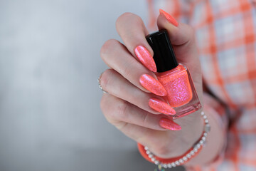 Woman hand with long nails and light orange coral neon manicure holds