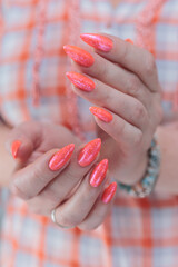 Woman hand with long nails and light orange coral neon manicure holds