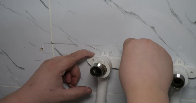 A close-up of a professional plumber's hands installing a corner faucet fitting on a marble-tiled wall. During a bathroom renovation, the plumber is installing a new faucet.