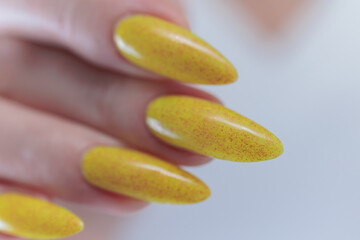 Female hand with long nails and a bottle of bright yellow orange nail polish	