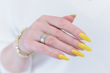 Female hand with long nails and a bottle of bright yellow orange nail polish	