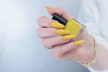 Female hand with long nails and a bottle of bright yellow orange nail polish	