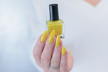 Female hand with long nails and a bottle of bright yellow orange nail polish	