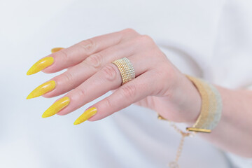 Female hand with long nails and a bottle of bright yellow orange nail polish	
